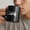 Black ceramic mug with “Shayan” Arabic calligraphy held by male model drinking coffee, minimalist lifestyle shot Pakistan