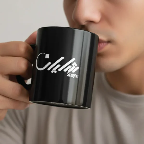 Black ceramic mug with “Shayan” Arabic calligraphy held by male model drinking coffee, minimalist lifestyle shot Pakistan